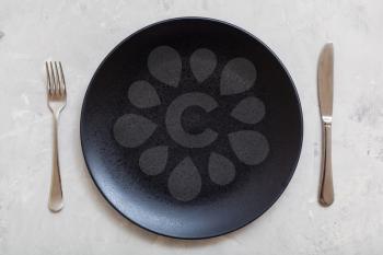 food concept - top view of black plate with knife, spoon on gray concrete surface