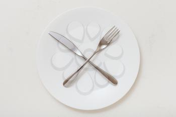 food concept - top view of white plate with crossing knife, spoon on white plastering board