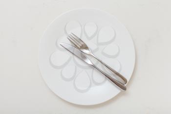 food concept - top view of white plate with parallel knife, spoon on white plastering board