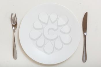 food concept - top view of white plate with knife, spoon on white plastering board