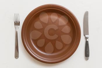 food concept - top view of brown plate with knife, spoon on white plastering board