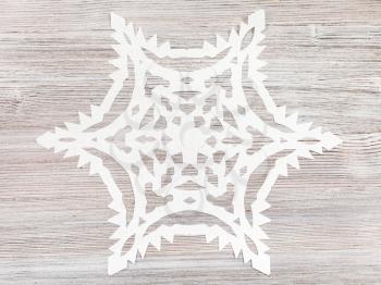 top view of snowflake carved from paper on light brown wooden surface