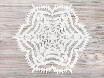 top view of snowflake carved from paper on light brown wooden table