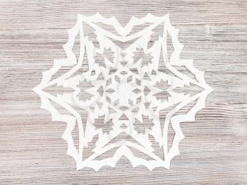 top view of snowflake carved from paper on light brown wooden plank