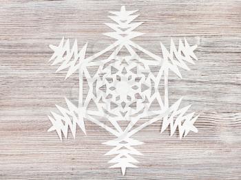 top view of snowflake carved from paper on light brown wooden board