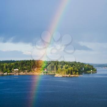 green island with settlement in Baltic Sea and rainbow in blue sky in sunny autumn day, Sweden