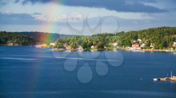 above view of green shore of Baltic Sea with village and rainbow in sunny autumn day, Sweden