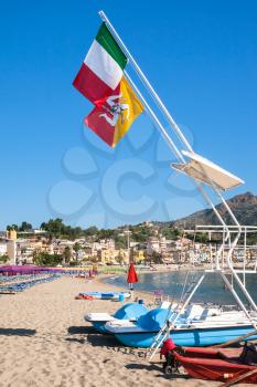 travel to Italy - Italian and Sicilian flags over urban beach of Giardini Naxos town in Sicily in morning