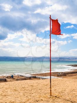 Travel to Middle East country Kingdom of Jordan - red flag on beach of Dead Sea in windy winter day