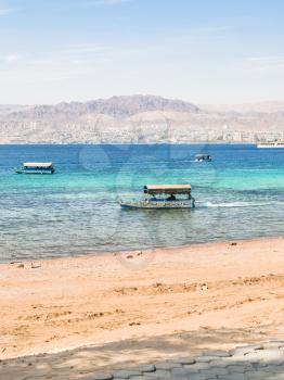 AQABA, JORDAN - FEBRUARY 23, 2012: boats near beach of Aqaba and view of Eilat city in background in winter. Jordan country has only one exit to sea in Gulf of Aqaba, the length of the coast is 27 km