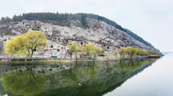 travel to China - view of carved West Hill with caves of Chinese Buddhist monument Longmen Grottoes (Dragon's Gate Grottoes, Longmen Caves) and bridge on Yi river in spring season