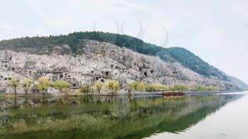 travel to China - panoramic view of West Hill with caves of Chinese Buddhist monument Longmen Grottoes (Dragon's Gate Grottoes, Longmen Caves) and bridge on Yi river in spring season