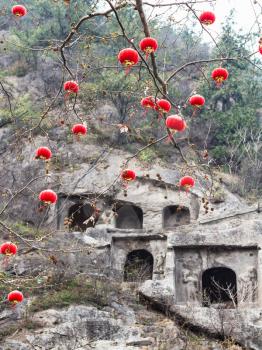 travel to China - chinese red lanterns of tree branches and view of caves on background in area of Longmen Grottoes (Longmen Shiku, Dragon's Gate Grottoes, Longmen Caves) in spring season