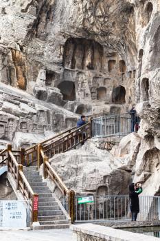 LUOYANG, CHINA - MARCH 20, 2017: tourists near carved rocks in Chinese Buddhist monument Longmen Grottoes (Longmen Caves). The complex was inscribed upon the UNESCO World Heritage List in 2000