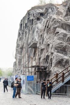 LUOYANG, CHINA - MARCH 20, 2017: visitors near carved rocks in Chinese Buddhist monument Longmen Grottoes (Longmen Caves). The complex was inscribed upon the UNESCO World Heritage List in 2000