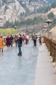LUOYANG, CHINA - MARCH 20, 2017: tourists at Manshui Bridge on Yi river between West and East Hills of Chinese Buddhist monument Longmen Grottoes ( Longmen Caves) in spring season