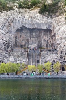 LUOYANG, CHINA - MARCH 20, 2017: View of West Hill of Chinese Buddhist monument Longmen Grottoes (Longmen Caves) with The Big Vairocana statue from the east bank of the Yi River in spring season