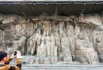 LUOYANG, CHINA - MARCH 20, 2017: tourist take photo of carved Buddha figure in Longmen Grottoes (Longmen Caves). The complex was inscribed upon the UNESCO World Heritage List in 2000