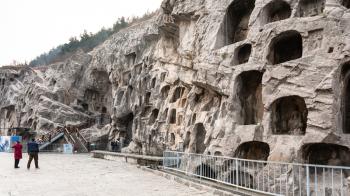 LUOYANG, CHINA - MARCH 20, 2017: tourists near caves in slope of West Hill of Chinese Buddhist monument Longmen Grottoes. The complex was inscribed upon the UNESCO World Heritage List in 2000