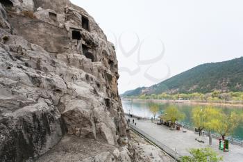 LUOYANG, CHINA - MARCH 20, 2017: above view of waterfront with tourists in Chinese Buddhist monument Longmen Grottoes. The complex was inscribed upon the UNESCO World Heritage List in 2000