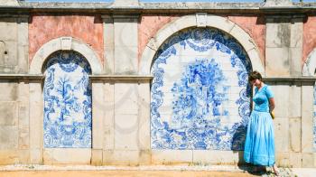 Travel to Algarve Portugal - tourist near outside wall of Estoi Palace with traditional azulejo tile decor in Estoi village. The Palace was built in the late 19th century