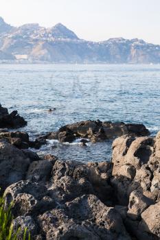 travel to Sicily, Italy - volcanic rocks on coast of Ionian sea in Giardini Naxos town in summer