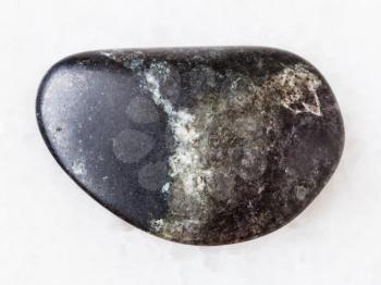 macro shooting of natural mineral rock specimen - tumbled olivinite stone on white marble background from Kovdor region, Kola Peninsula, Russia