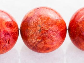 macro shooting of natural mineral rock specimen - beads from red Coral gemstone on white marble background