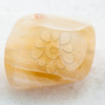 macro shooting of natural mineral rock specimen - tumbled yellow banded Agate gemstone on white marble background