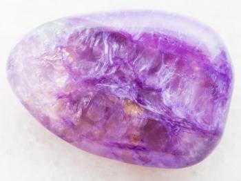 macro shooting of natural mineral rock specimen - tumbled Charoite gemstone on white marble background from Sakha Republic, Siberia, Russia
