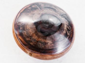 macro shooting of natural mineral rock specimen - polished bead from brown Agate gemstone on white marble background