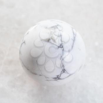 macro shooting of natural mineral rock specimen - ball from Howlite gemstone on white marble background