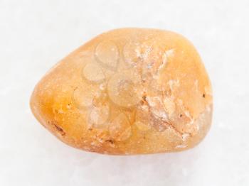 macro shooting of natural mineral rock specimen - tumbled yellow chalcedony stone on white marble background
