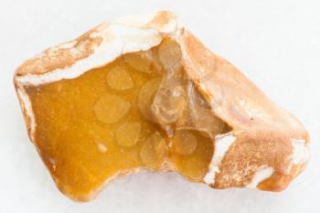 macro shooting of natural mineral rock specimen - pebble of yellow Flint stone on white marble background