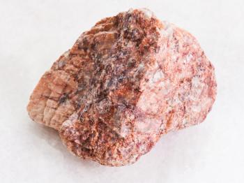 macro shooting of natural mineral rock specimen - raw pink Granite stone on white marble background from Brittany
