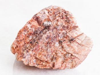 macro shooting of natural mineral rock specimen - piece of pink Granite stone on white marble background from Brittany