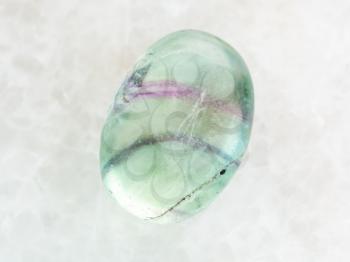 macro shooting of natural mineral rock specimen - tumbled Fluorite gemstone on white marble background