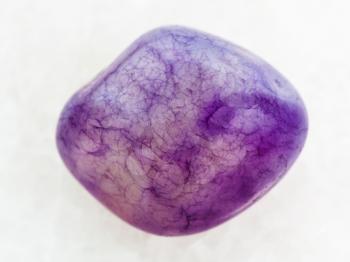 macro shooting of natural mineral rock specimen - tumbled Amethyst crystal gem on white marble background