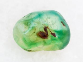 macro shooting of natural mineral rock specimen - tumbled green dyed agate gemstone on white marble background