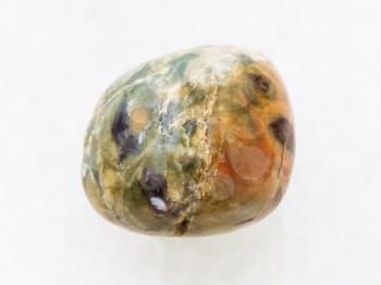 macro shooting of natural mineral rock specimen - polished rhyolite rainforest jasper gemstone on white marble background