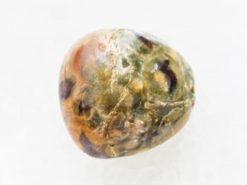 macro shooting of natural mineral rock specimen - tumbled rhyolite rainforest jasper gemstone on white marble background