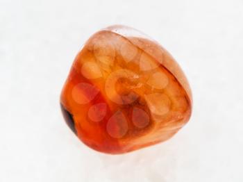 macro shooting of natural mineral rock specimen - tumbled carnelian gem stone on white marble background