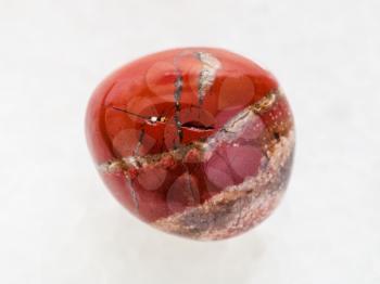 macro shooting of natural mineral rock specimen - tumbled red Jasper gem stone on white marble background