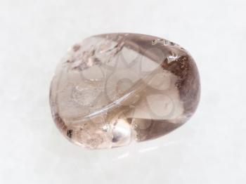 macro shooting of natural mineral rock specimen - tumbled smoky quartz gemstone on white marble background