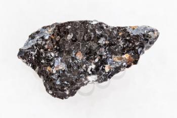 macro shooting of natural mineral rock specimen - raw obsidian (volcanic glass) stone on white marble background