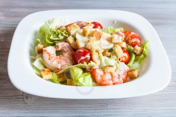 Caesar salad with prawns on white plate on gray wooden table