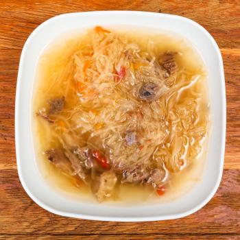 top view of traditional russian soup with stewed sour cabbage in white plate on wooden table
