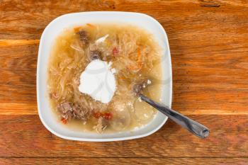 top view of traditional russian cabbage soup with stewed sauerkraut and sour cream in ceramic plate on wooden table