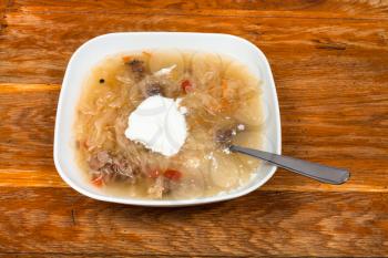 russian cabbage soup with stewed sauerkraut and sour cream in ceramic plate on wooden table