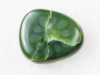 macro shooting of natural mineral rock specimen - polished green nephrite gemstone on white marble background